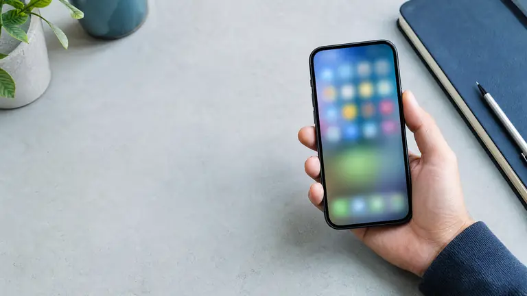 A smartphone displaying a simple, uncluttered home screen beside a notebook and headphones.
